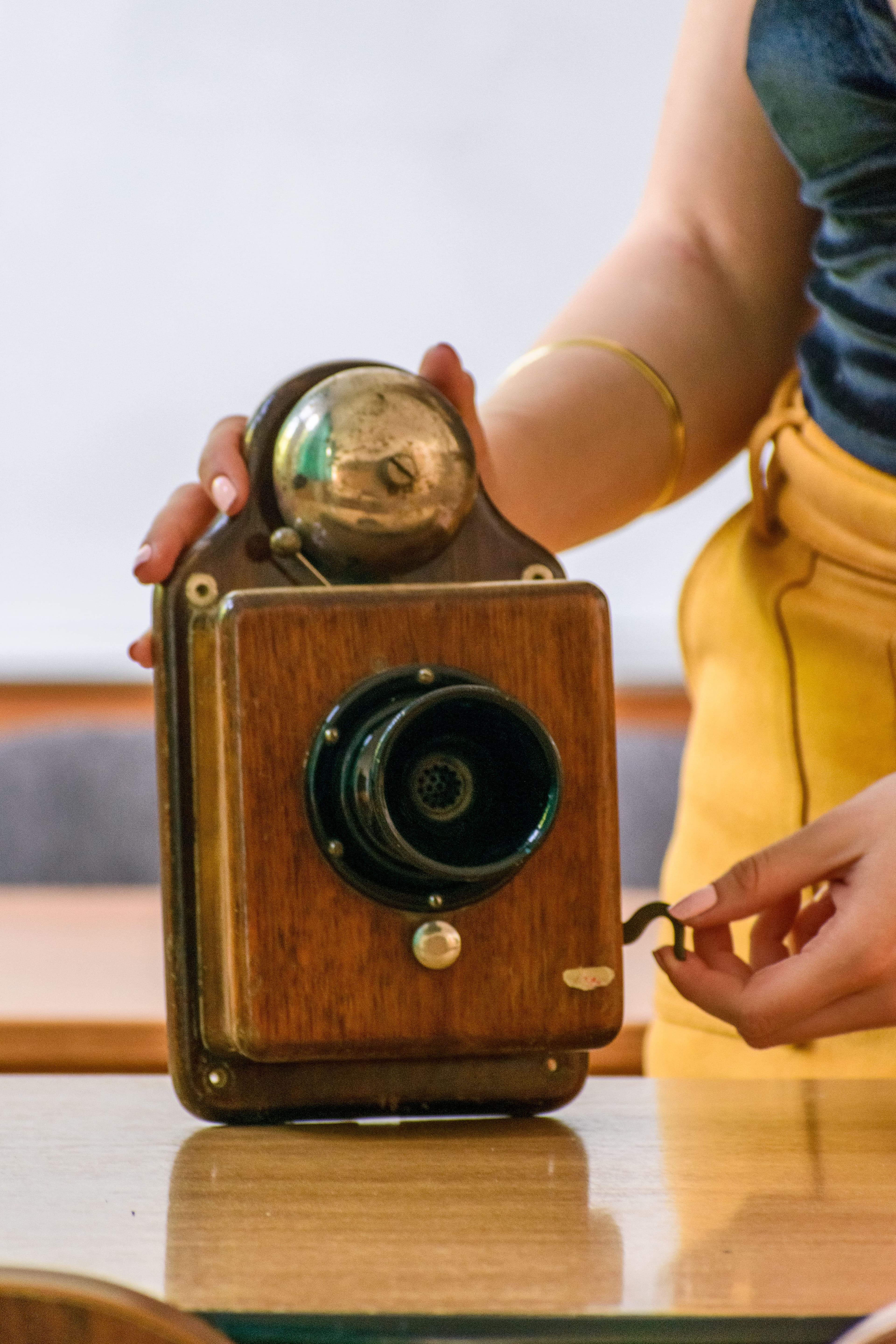 A hand touching an old wall-mounted phone with a clock.